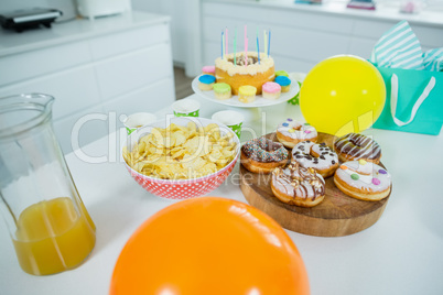 Doughnuts, potato chip, birthday cake and balloons on table