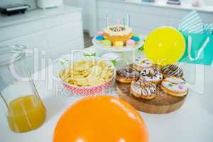 Doughnuts, potato chip, birthday cake and balloons on table