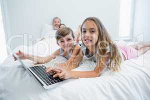 Smiling girl and boy using laptop on bed in bedroom at home