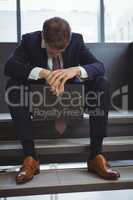 Depressed businessman with clipboard sitting on stairs