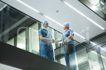 Male surgeons shaking hands in corridor