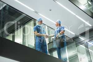 Male surgeons shaking hands in corridor