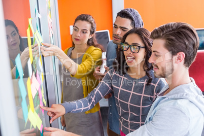 Smiling executives discussing over sticky notes on glass wall