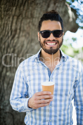 Handsome man in sunglasses holding disposable coffee cup in the park