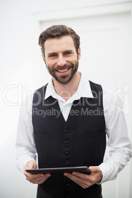 Male waiter smiling while holding digital tablet in the restaurant