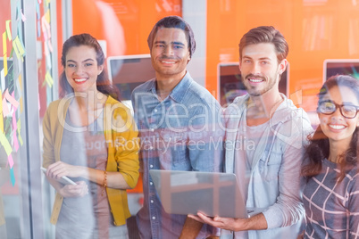 Portrait of smiling executives discussing over sticky notes on glass wall