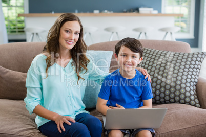 Portrait of smiling mother and son sitting on sofa using laptop