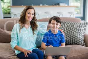 Portrait of smiling mother and son sitting on sofa using laptop