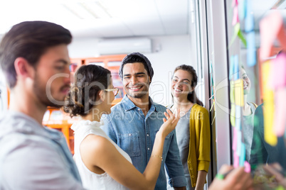 Smiling executives discussing over sticky note on glass wall