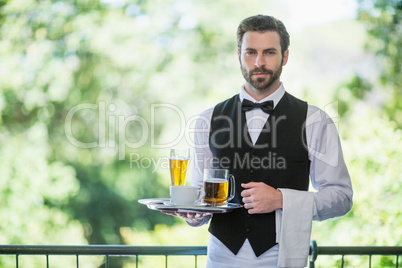 Male waiter holding tray with beer glass and coffee cup in restaurant