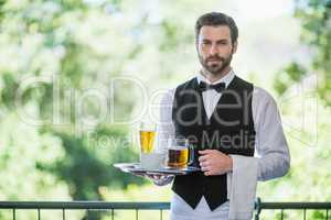 Male waiter holding tray with beer glass and coffee cup in restaurant