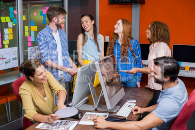 Smiling graphic designers interacting with each other while working at desk