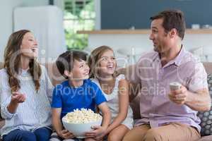 Family watching tv and eating popcorn in living room at home