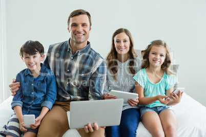 Smiling family using laptop, digital tablet and mobile phone in bedroom