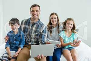 Smiling family using laptop, digital tablet and mobile phone in bedroom