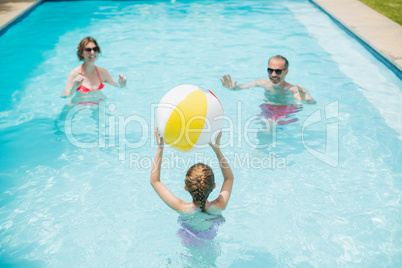 Happy parents and daughter playing with swim ball in swimming pool