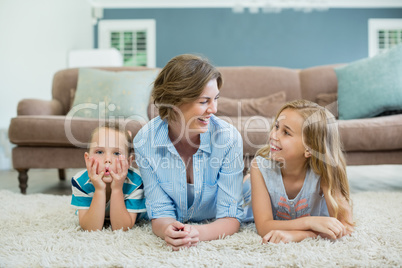 Smiling mother with her son and daughter lying on carpet in living room