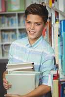 Portrait of schoolboy holding books in library