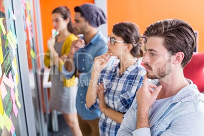 Thoughtful executives reading sticky notes on glass wall