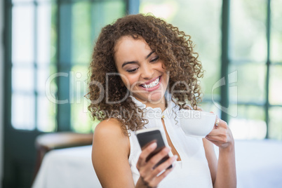 Beautiful woman holding coffee cup and using mobile phone