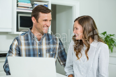 Happy couple interacting with each other while using laptop in living room