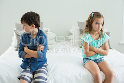 Sad siblings sitting with arms crossed in bedroom