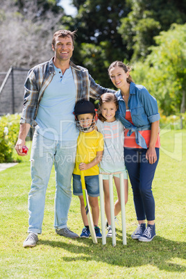 Portrait of happy family playing cricket together in backyard
