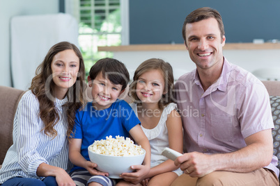 Smiling family watching tv and eating popcorn in living room at home