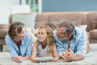 Happy family using digital tablet while lying on floor in living room