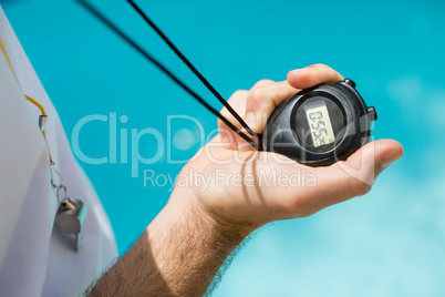 Mid section of swim coach holding stopwatch near poolside
