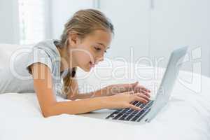 Smiling girl lying on bed and using laptop in bedroom