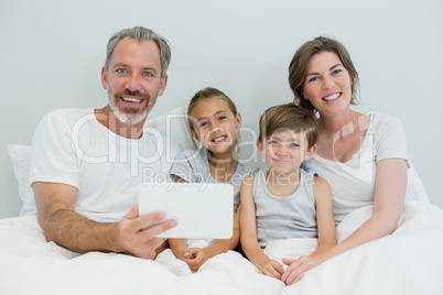Happy family using digital tablet on bed in bedroom at home