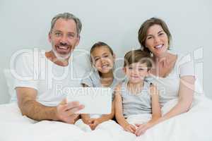 Happy family using digital tablet on bed in bedroom at home