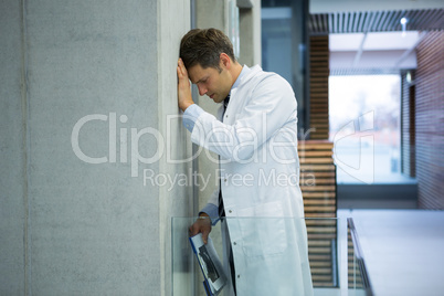 Worried male doctor leaning on wall near corridor