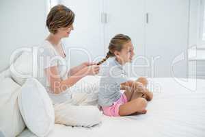 Smiling mother combing daughters hair on bed in bedroom