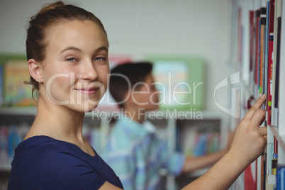Schoolgirl selecting book from book shelf in library at school