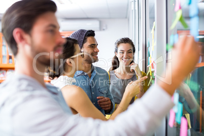 Smiling executives writing on sticky notes on glass wall