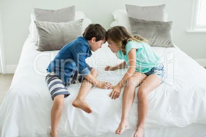 Angry brother and sister face to face on bed in bedroom
