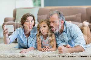 Family taking selfie from mobile phone while lying together on carpet in living room