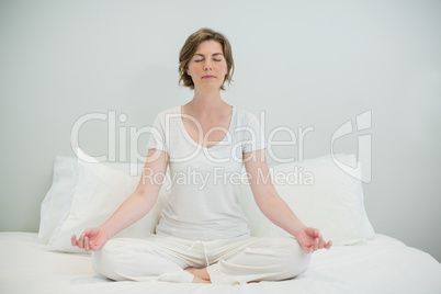 Woman doing meditation on bed in bedroom