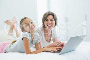 Smiling mother and daughter using laptop on bed