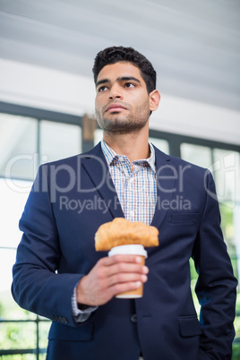 Businessman holding disposable coffee cup and croissant in a restaurant