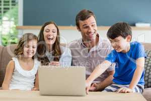 Family sitting on sofa using laptop in living room at home