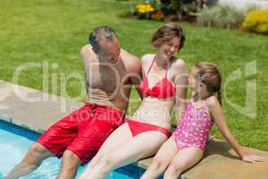 Happy parents and daughter sitting on poolside in pool water
