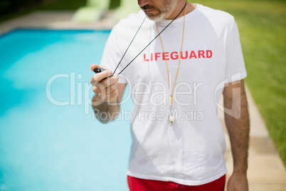 Swim coach looking at stop watch near poolside on a sunny day