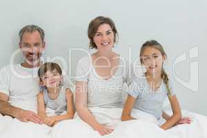 Happy family sitting together on bed in bedroom at home