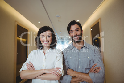 Portrait of male and female business executives standing with arms crossed in corridor