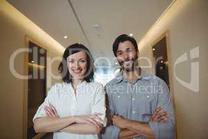 Portrait of male and female business executives standing with arms crossed in corridor