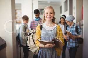 Portrait of smiling schoolgirl standing with notebook in corridor