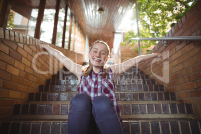 Portrait of happy schoolgirl sitting with arms outstretched on staircase